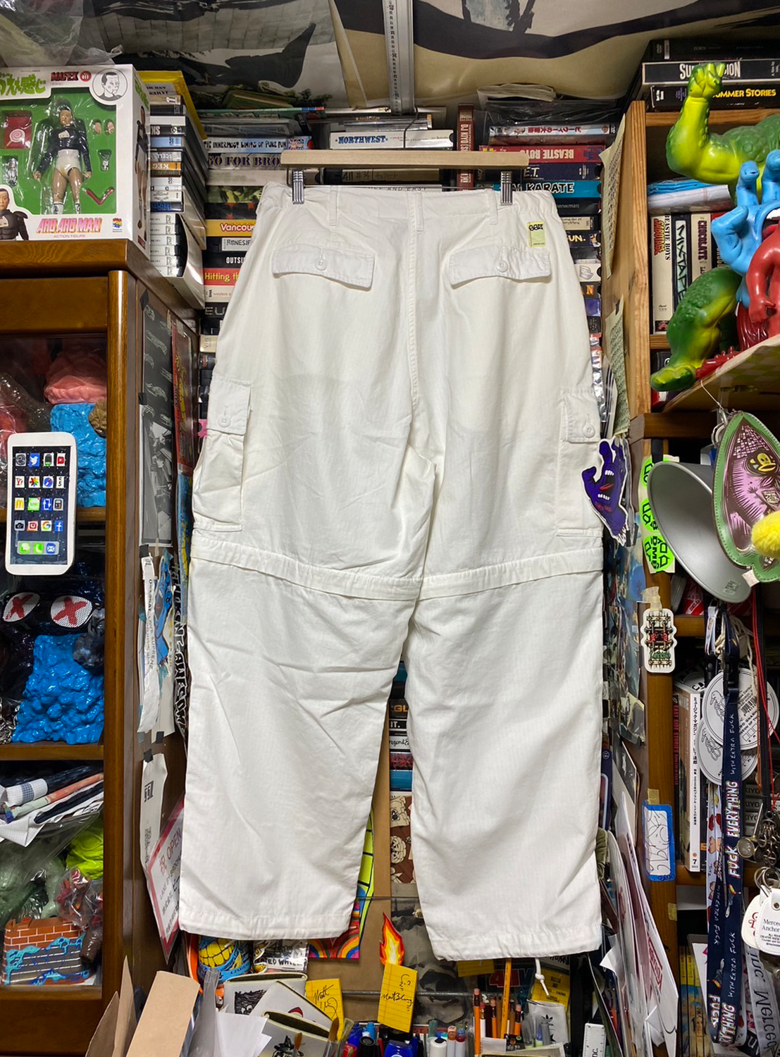 Back view of a pair of white SSZ FE Getto 6PK Pants hanging on a display hanger, surrounded.