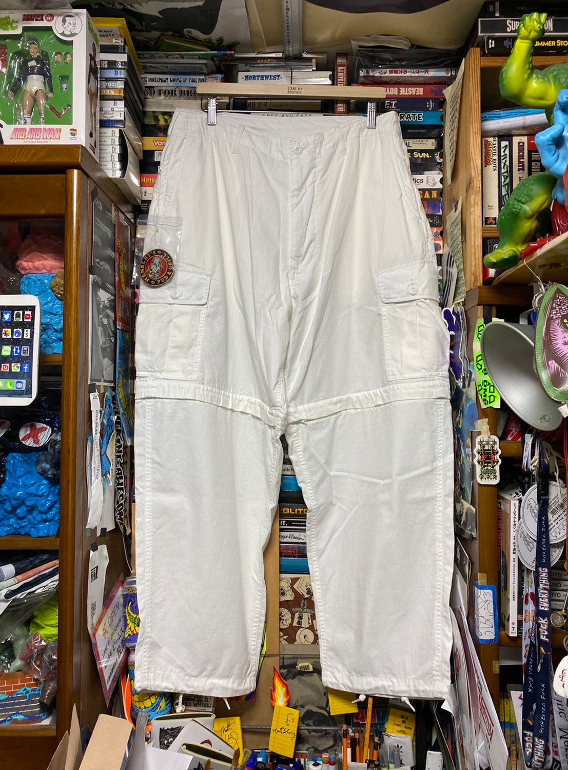 Front view of a pair of white SSZ FE Getto 6PK Pants hanging on a display hanger, surrounded.