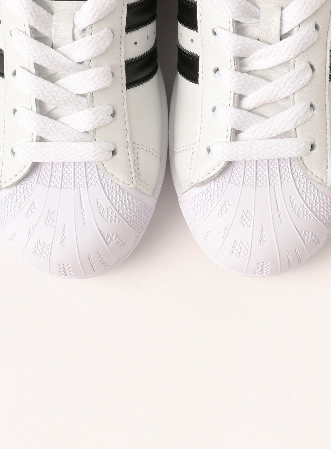 Close-up of two adidas SUPERSTAR II White men's sneakers with textured rubber toe caps and black stripes, side by side on a light background—an exclusive adidas release.