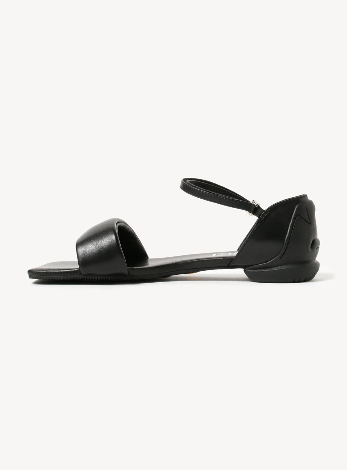 Black flat sandal, shown from the side, with a visible ankle strap and toe strap.