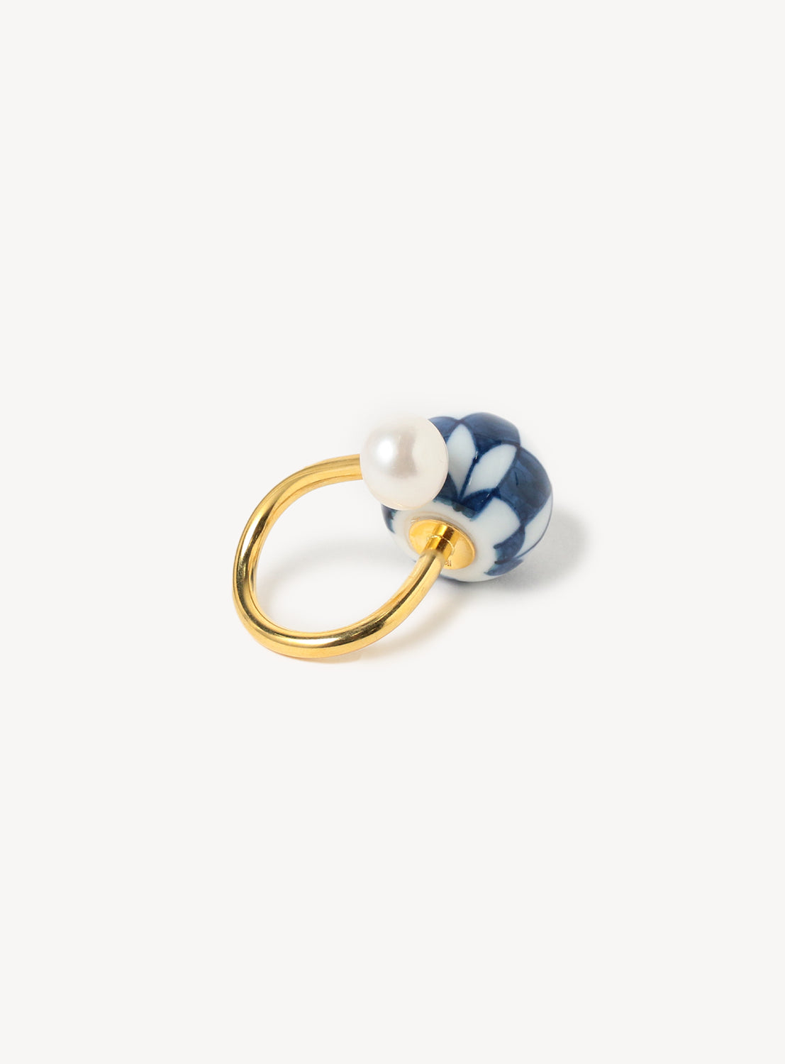Back view of a gold ring with a blue and white checkered patterned bead and a pearl embellishment.