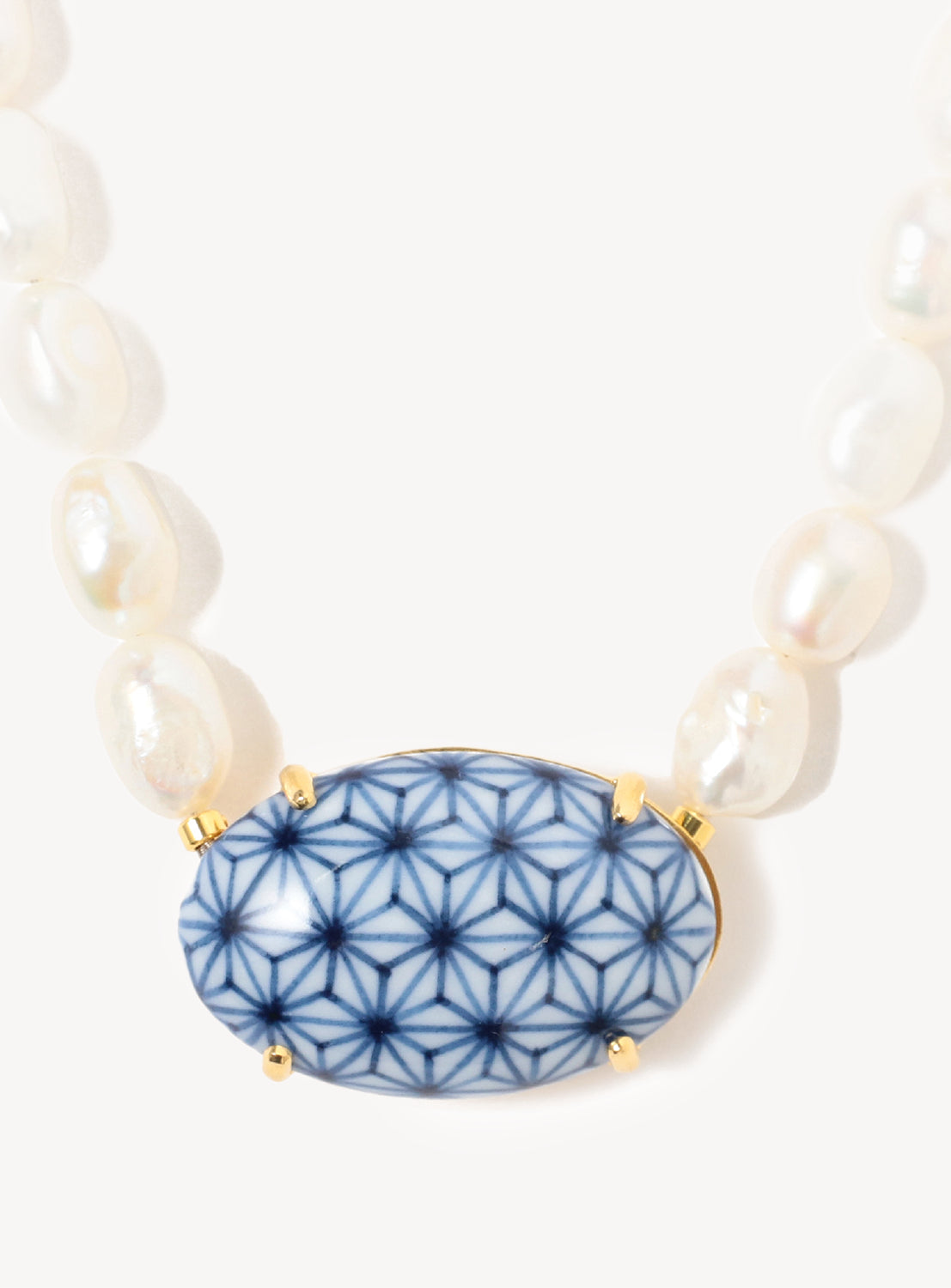 Close up short necklace with white pearls and a blue and white leaf-pattern motif pendant.