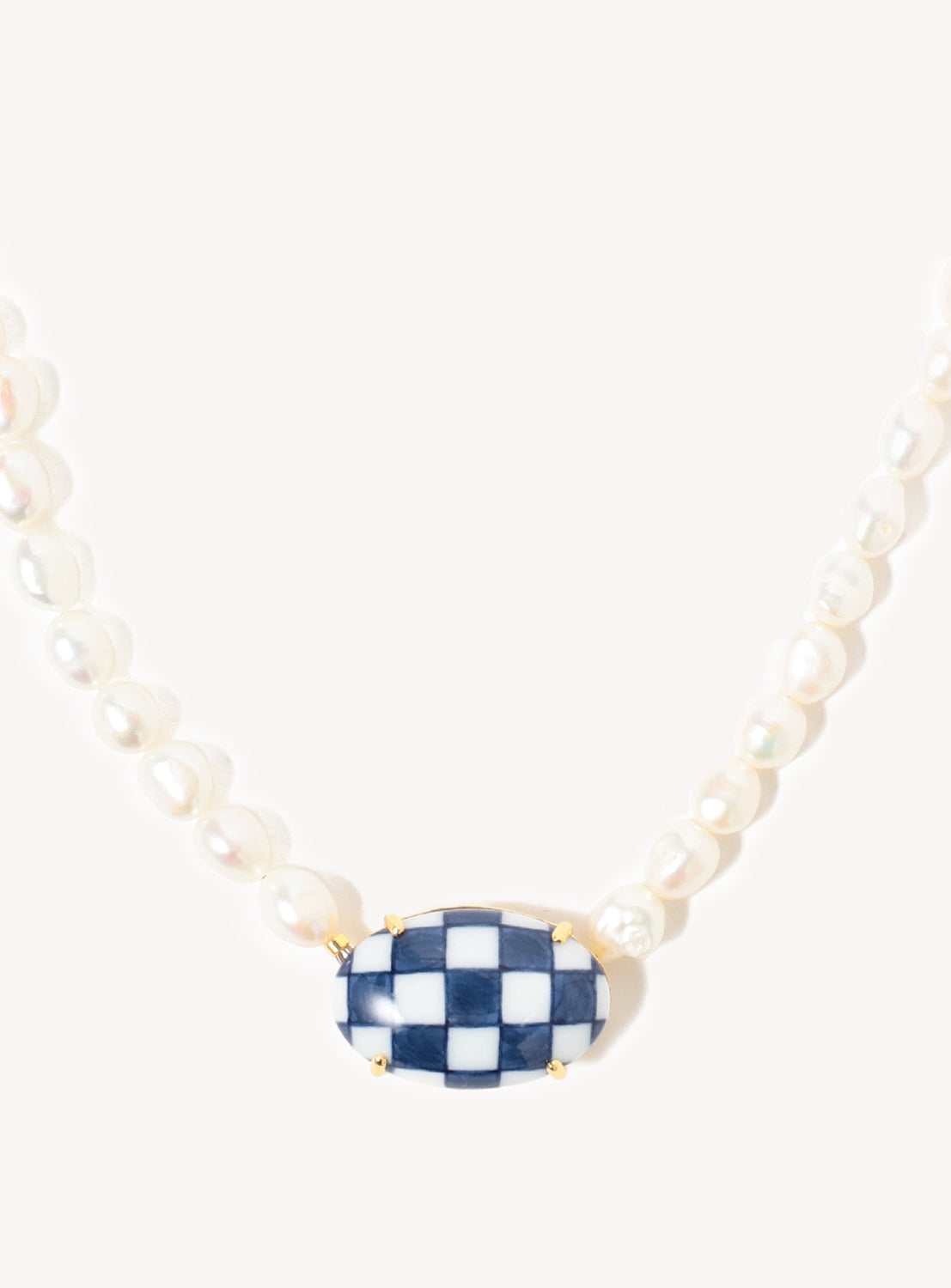 Close up of the long pearl necklace with a checkered blue and white ceramic pendant.