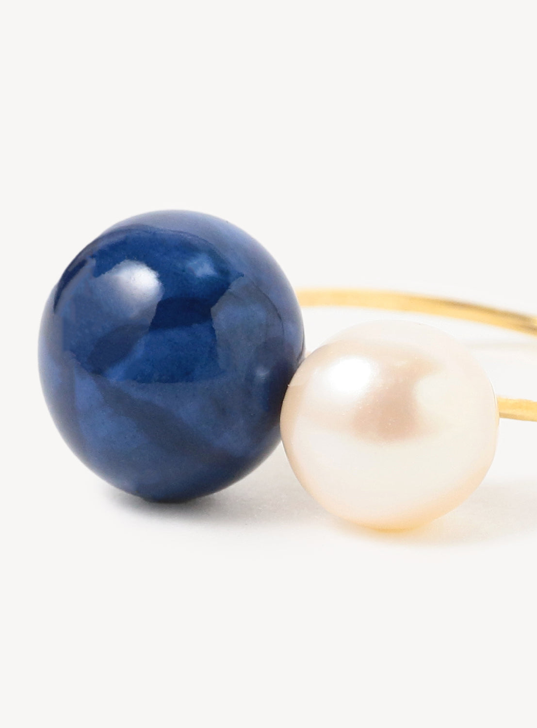 A close up of gold ring with one large blue bead and one large white pearl set horizontally.