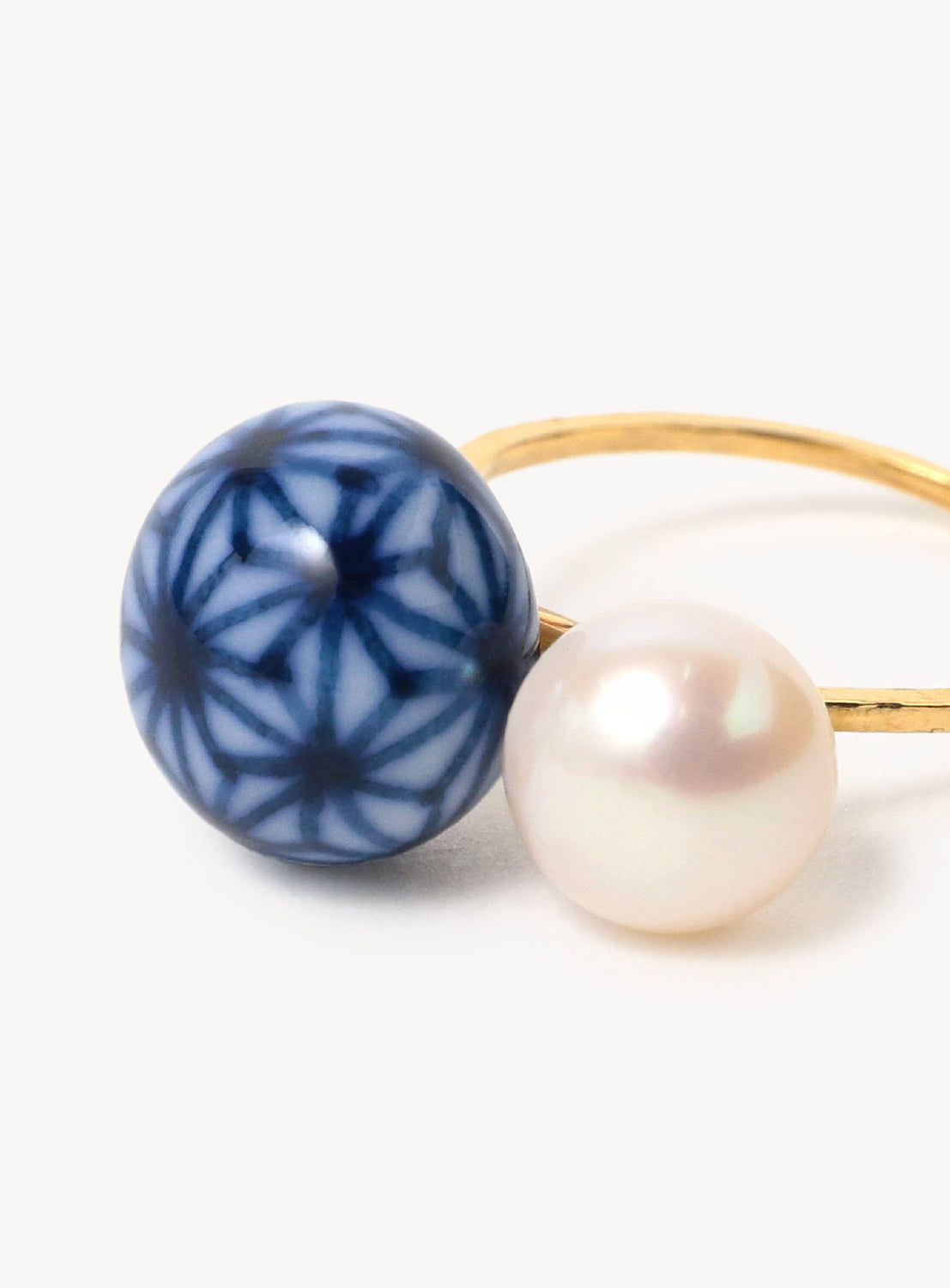 Close up of a gold ring featuring a blue and white ceramic round stone and a white pearl.
