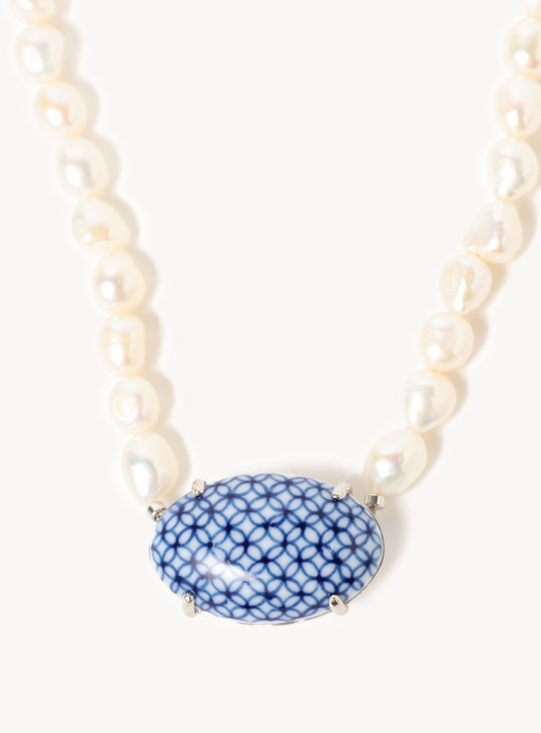 Close up of a short necklace with white pearls and a blue and white ceramic pendant.