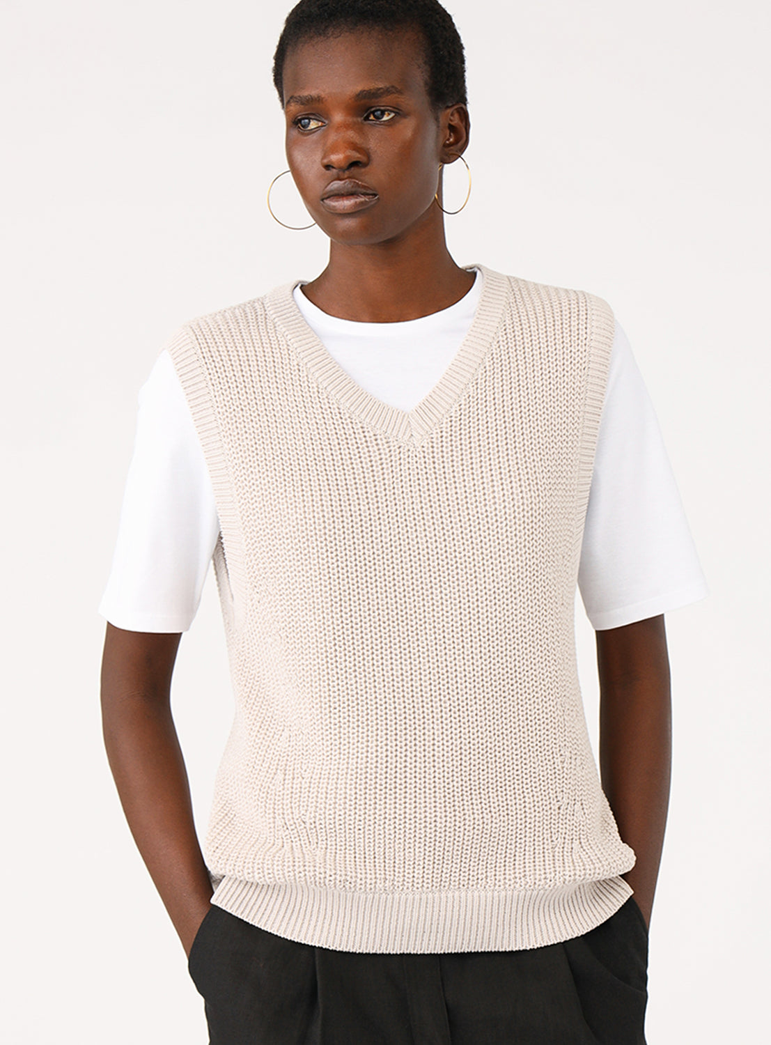 Model showcasing the front of a light grey colored V-neck knit sweater vest.
