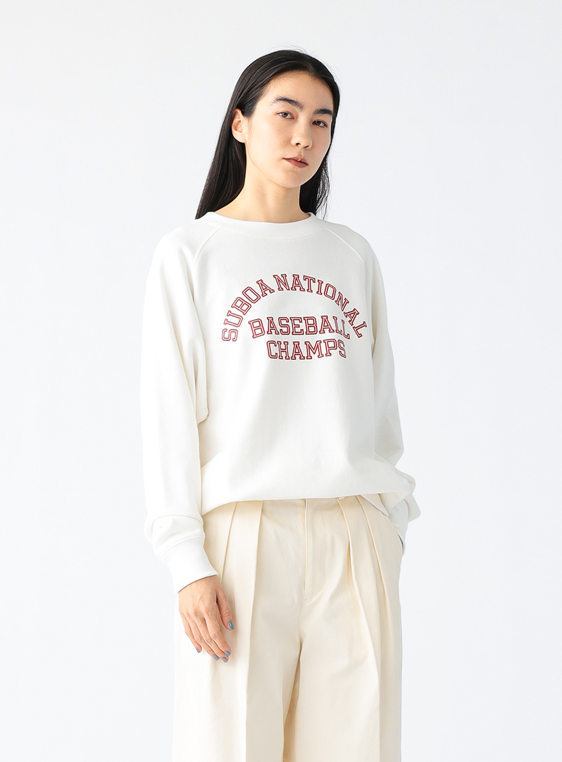A model wearing a white crewneck sweatshirt with the text 'SUDA NATIONAL BASEBALL CHAMPS' printed in red on the front.