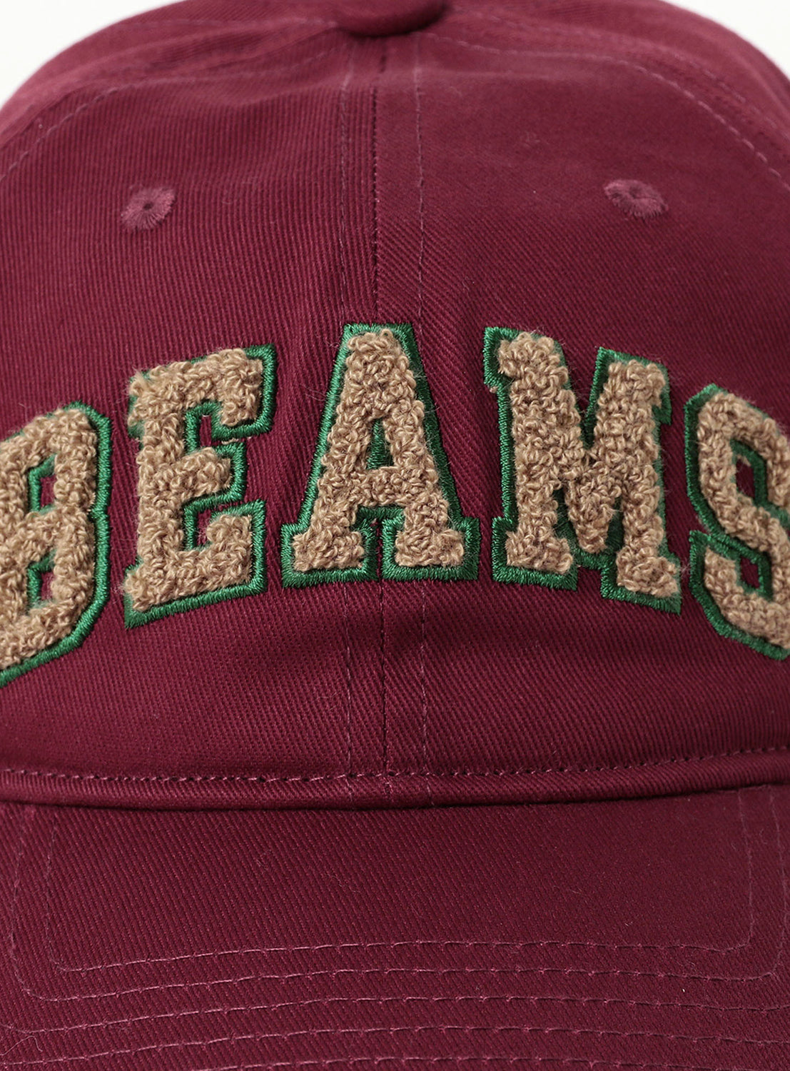 Close up of burgundy cap with embroidered beige and green 'BEAMS' text.