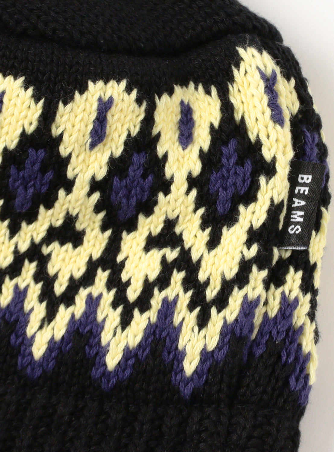 Close up of a black knit beanie with yellow jacquard pattern.