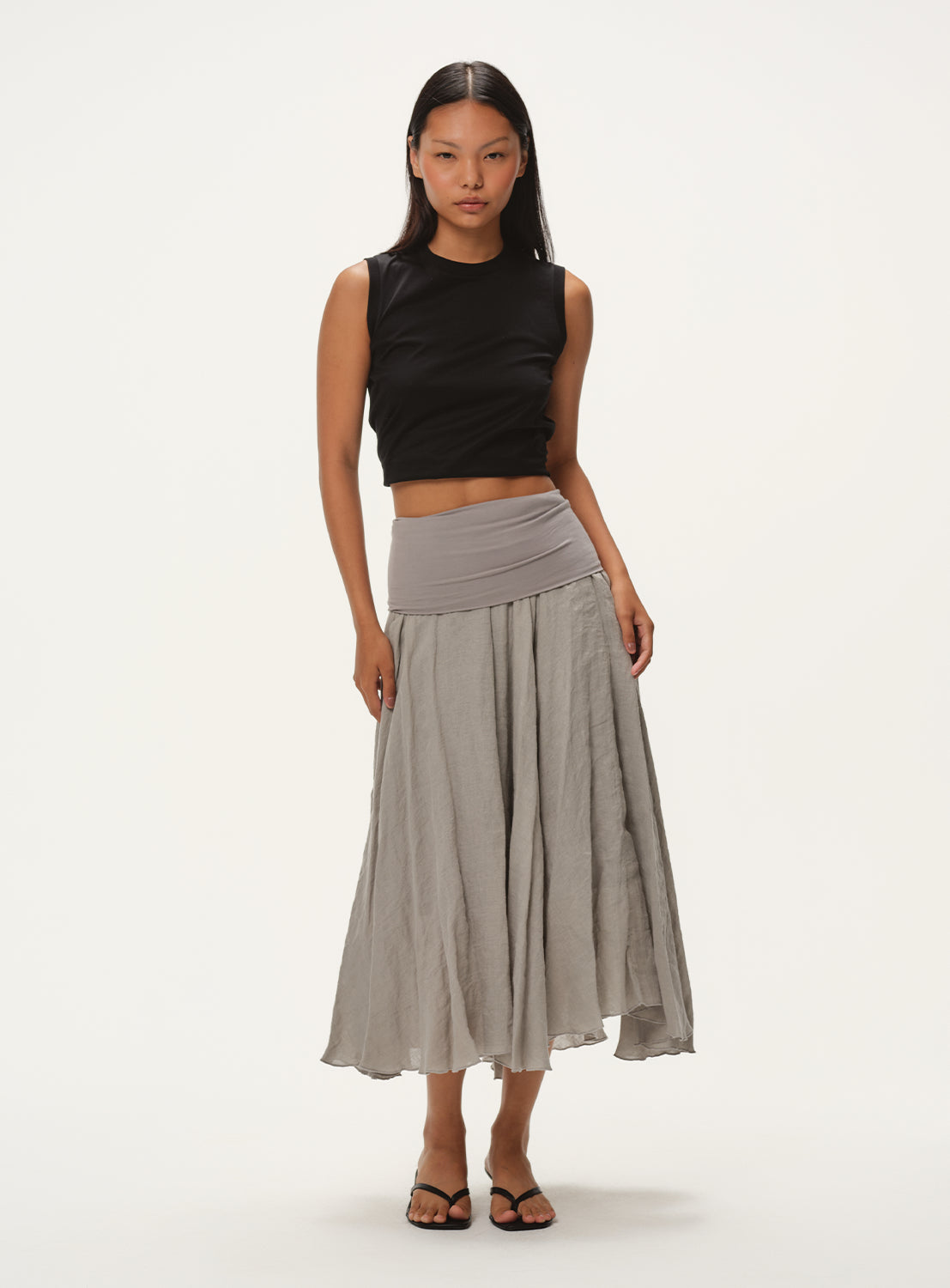 A female model wearing a light grey, full midi skirt with a black sleeveless crop top, standing facing forward.