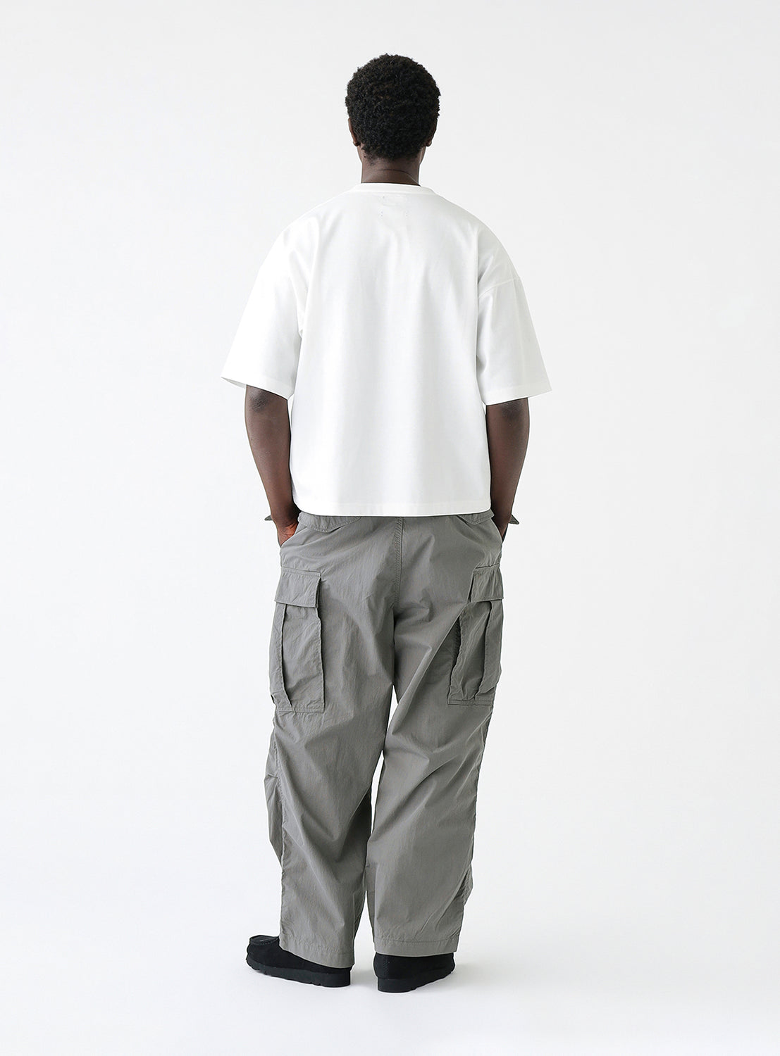 Back view of a model wearing a pair of gray cargo pants with multiple pockets, styled.