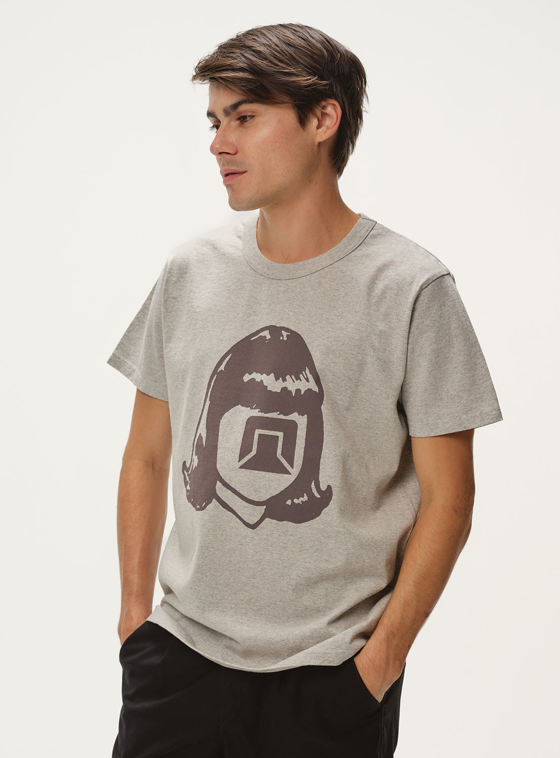 Model wearing a light grey t-shirt with a stylized face graphic and black pants, front view, displaying casual fit.