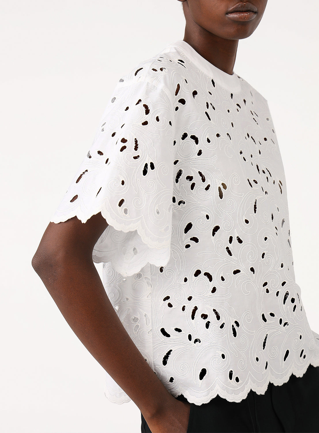 Close-up of a model wearing a white blouse, highlighting the intricate cutwork embroidery and simple silhouette.