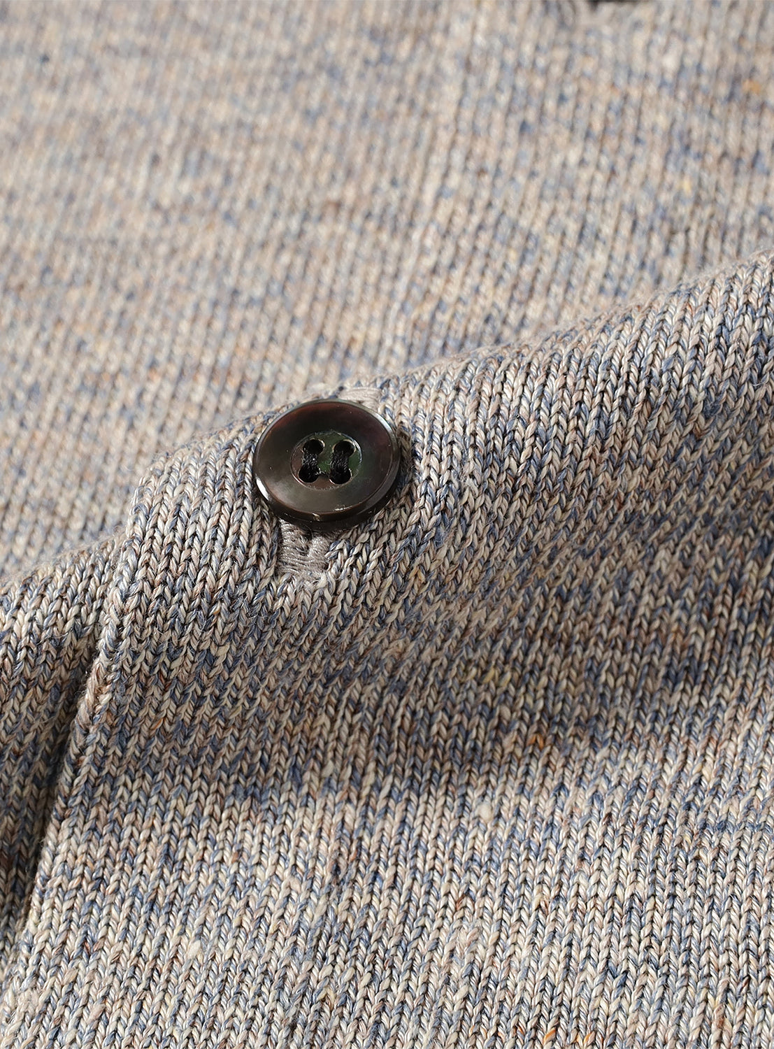 Close-up of light grey shirt fabric, showing texture and a single dark button.