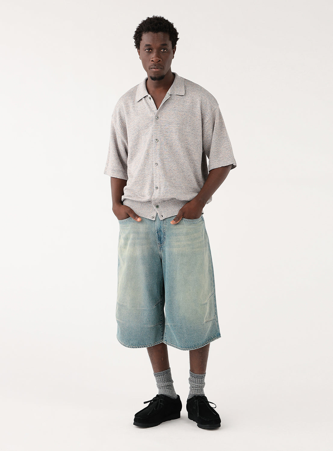 Male model wearing a light grey, short-sleeved collared shirt and light denim shorts.