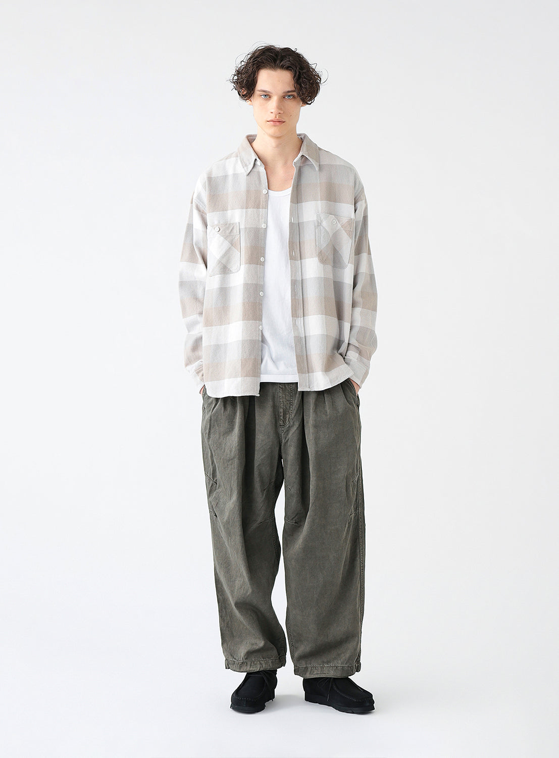 Full body view of a model wearing a beige and white check flannel shirt with long sleeves, two front pockets and a collar.