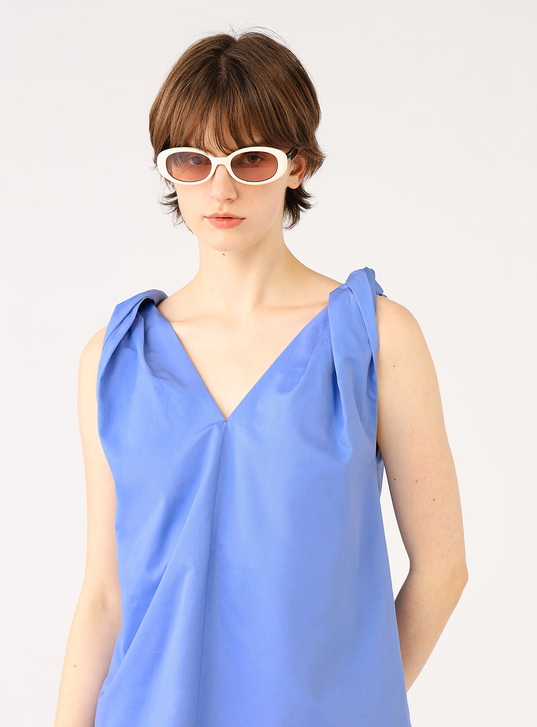 Close-up of a model wearing a blue V-neck top with pleated shoulder straps.