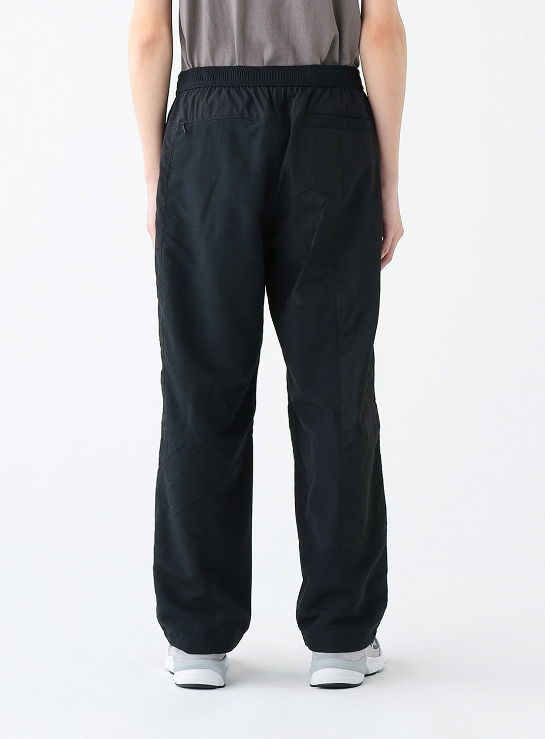 Close up back view of a model wearing a pair of black track pants.