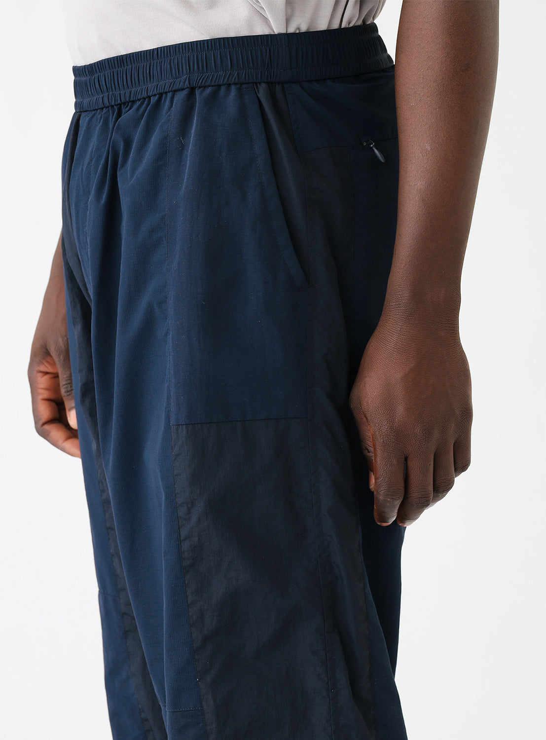 Close up side view of a model wearing a pair of navy blue track pants, highlighting the pocket and different color detais.
