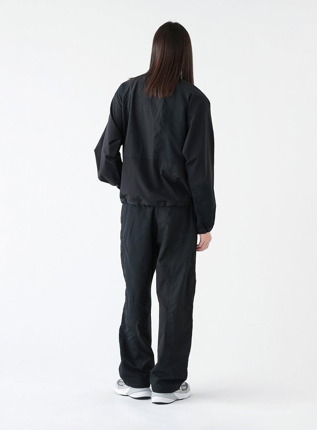 Back view of a model wearing a pair of black track pants, styled.