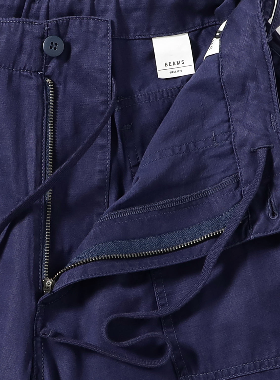 Texture close-up of navy blue cargo pants, highlighting the zipper, button closure and drawstrings.