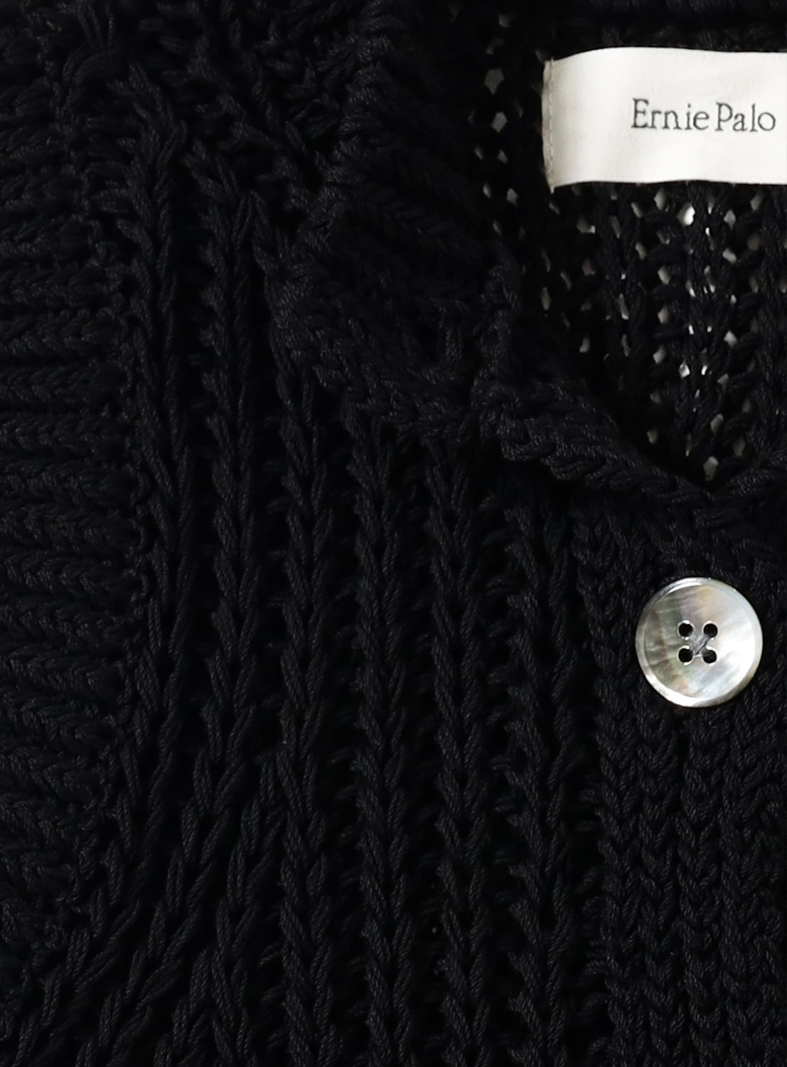 Close-up of a black knit textured garment with a button and 'Ernie Palo' label.