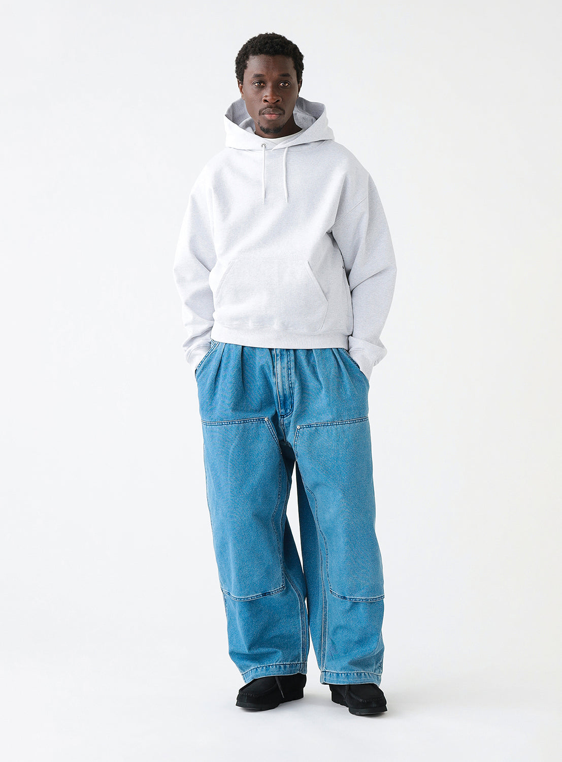 Model wearing a pair of faded blue denim double-knee painter pants styled with a light grey hoodie.