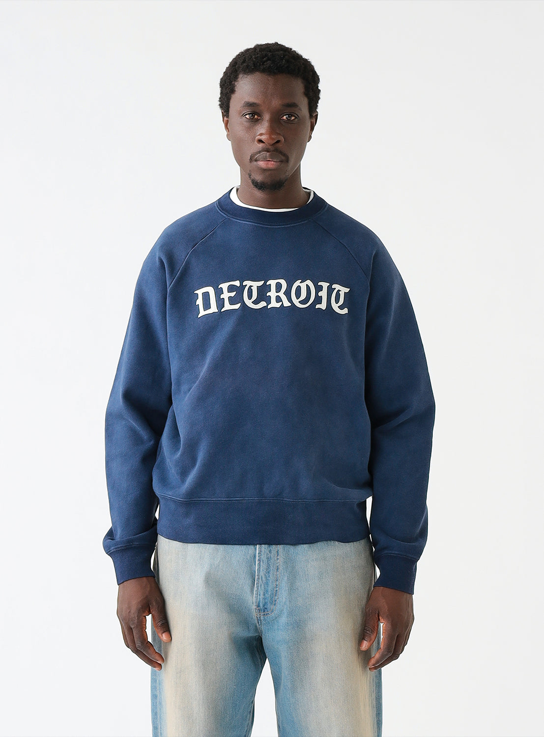 A model wearing a navy blue crew neck sweatshirt with the word 'DETROIT' printed in white on the front.