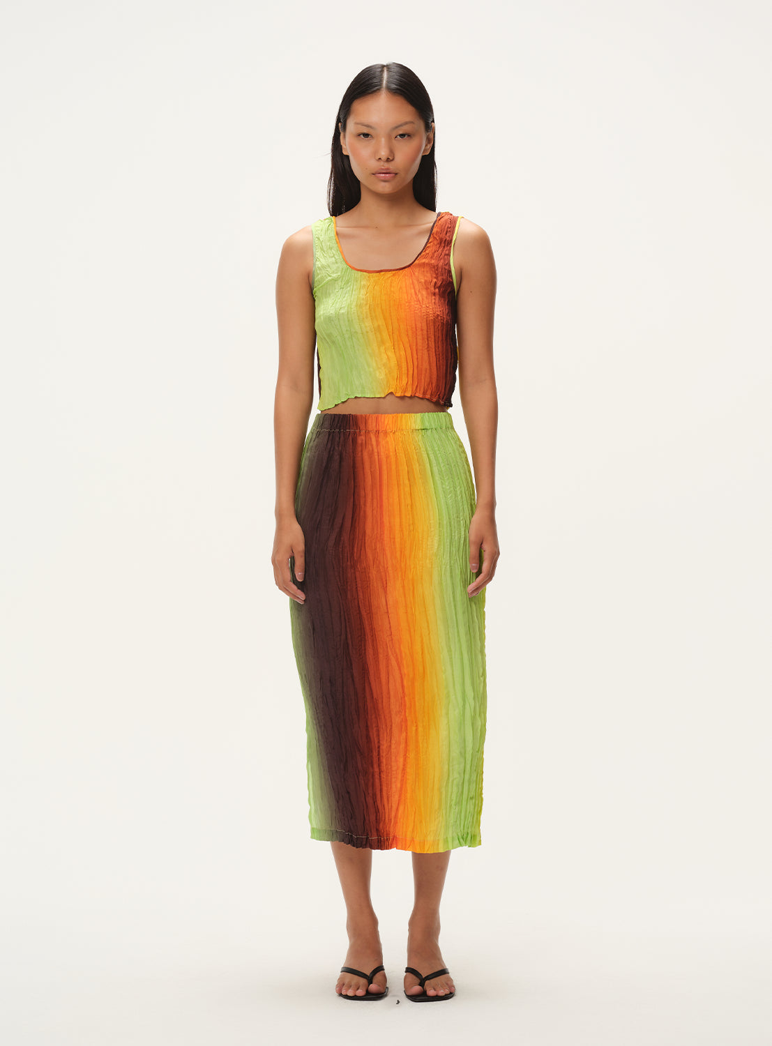 A front-facing view of a woman wearing a vertically striped knit midi skirt and a matching sleeveless top, standing.