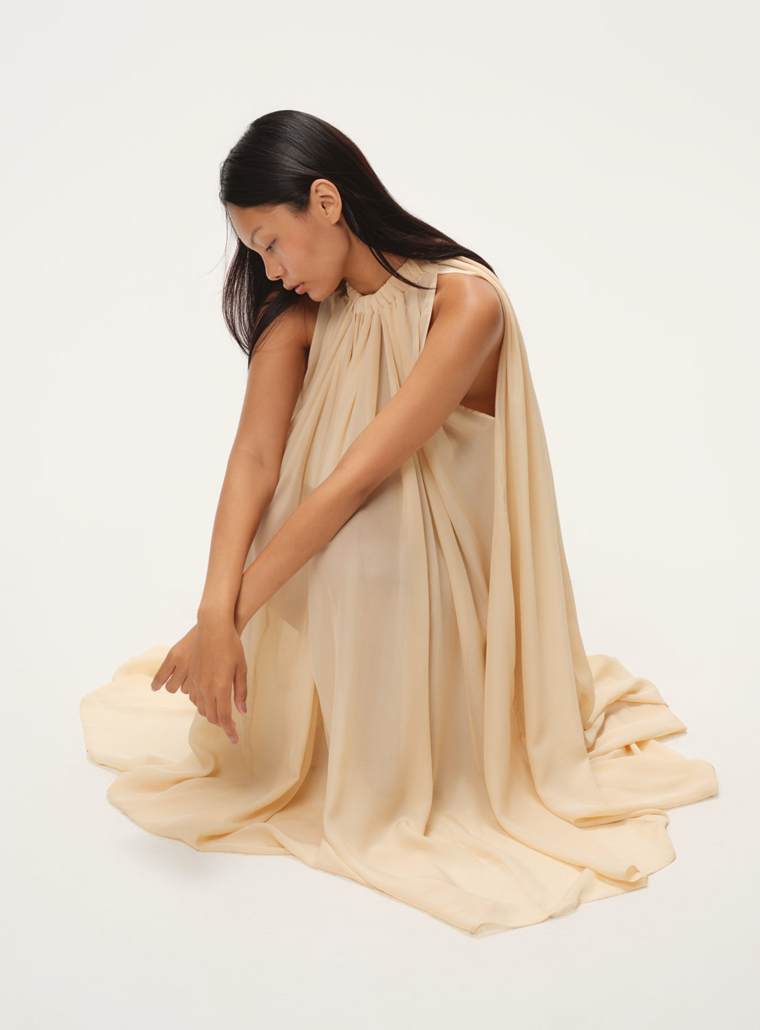 Model wearing a beige flowy silk dress with a draped design and a high neck.