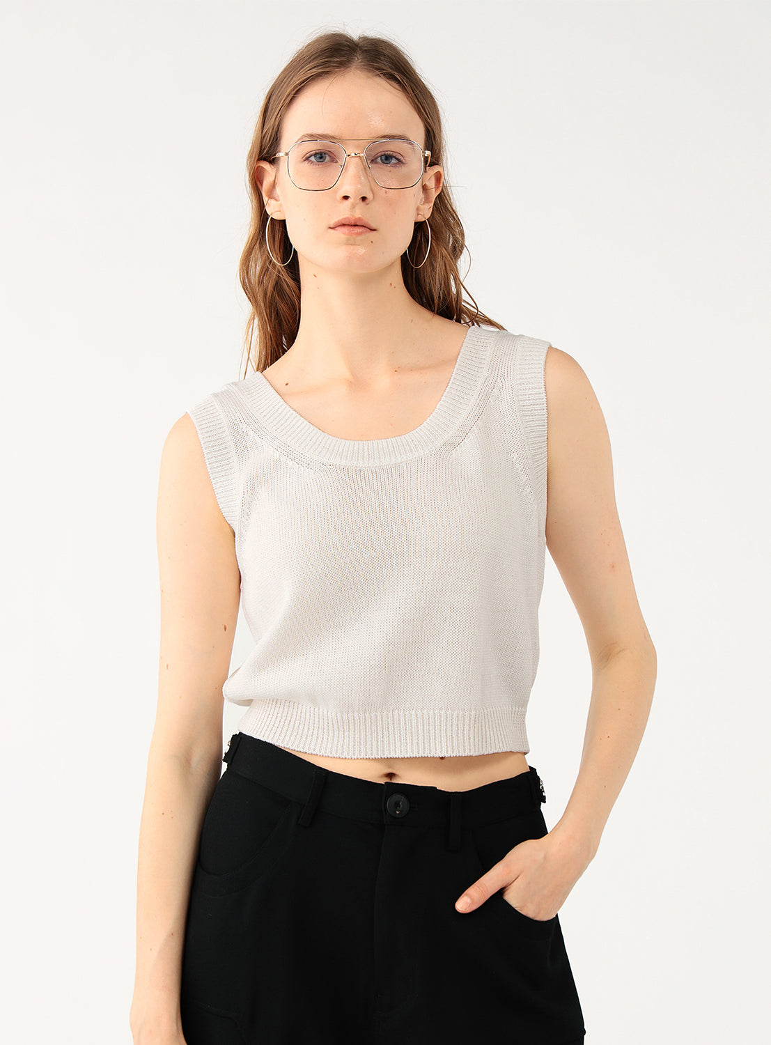 Full body shot of a model wearing a white knit top, styled with a black skirt and glasses.