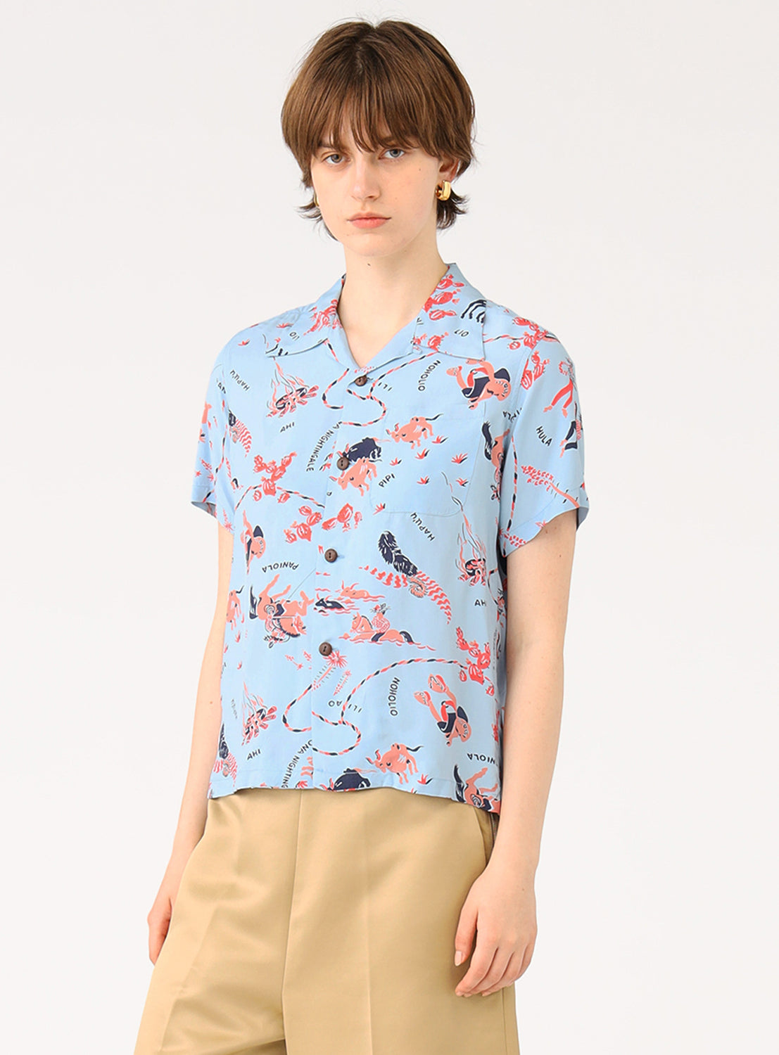 Full body shot of a model wearing a light blue patterned shirt, styled with khaki shorts.