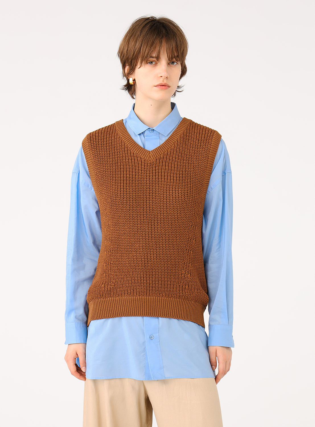 Model wearing a brown camel knit vest layered over a blue collared shirt and beige pants.
