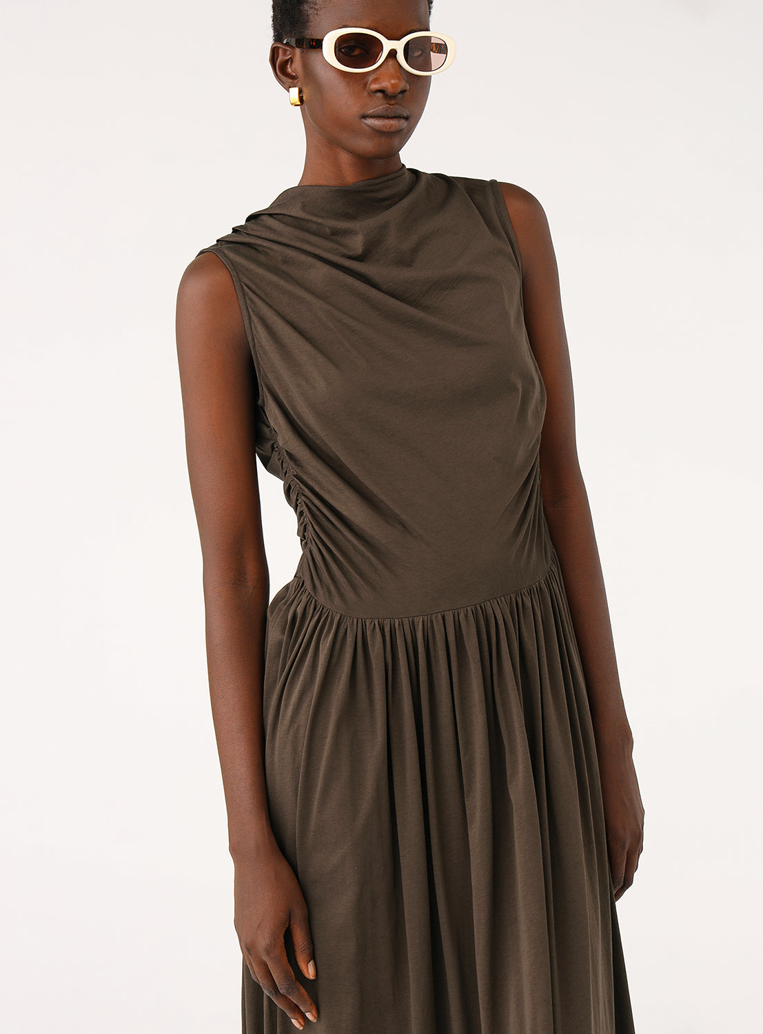 Close-up of the model, focusing on the high draped neckline and the pleating on the bodice of the brown dress.