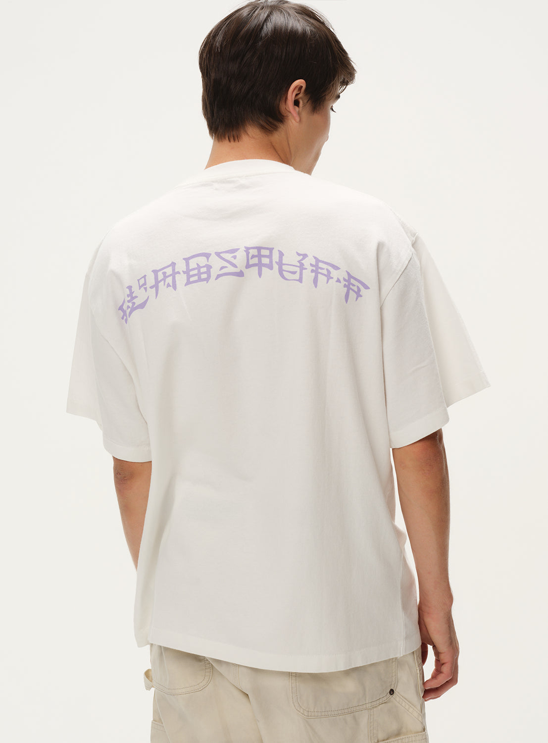 Model wearing a white t-shirt, back view, showcasing the purple text graphic print on the upper back.