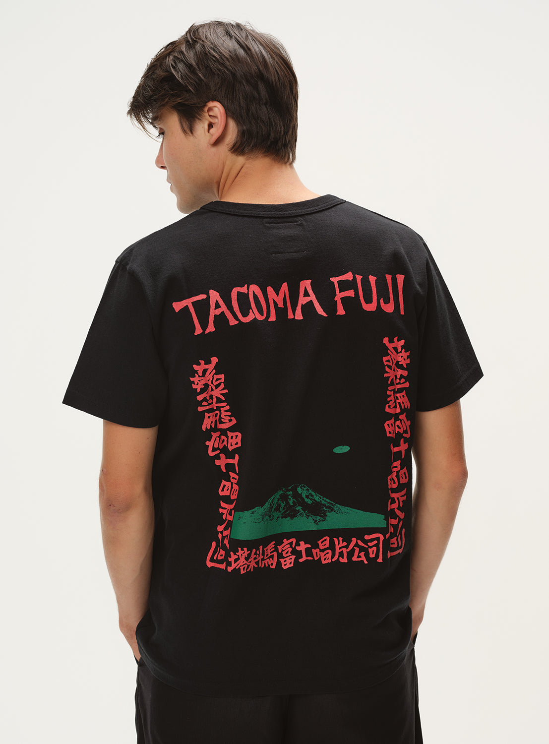 Model wearing a black t-shirt, back view, showcasing red "TACOMA FUJI" graphic with green details and Japanese characters.