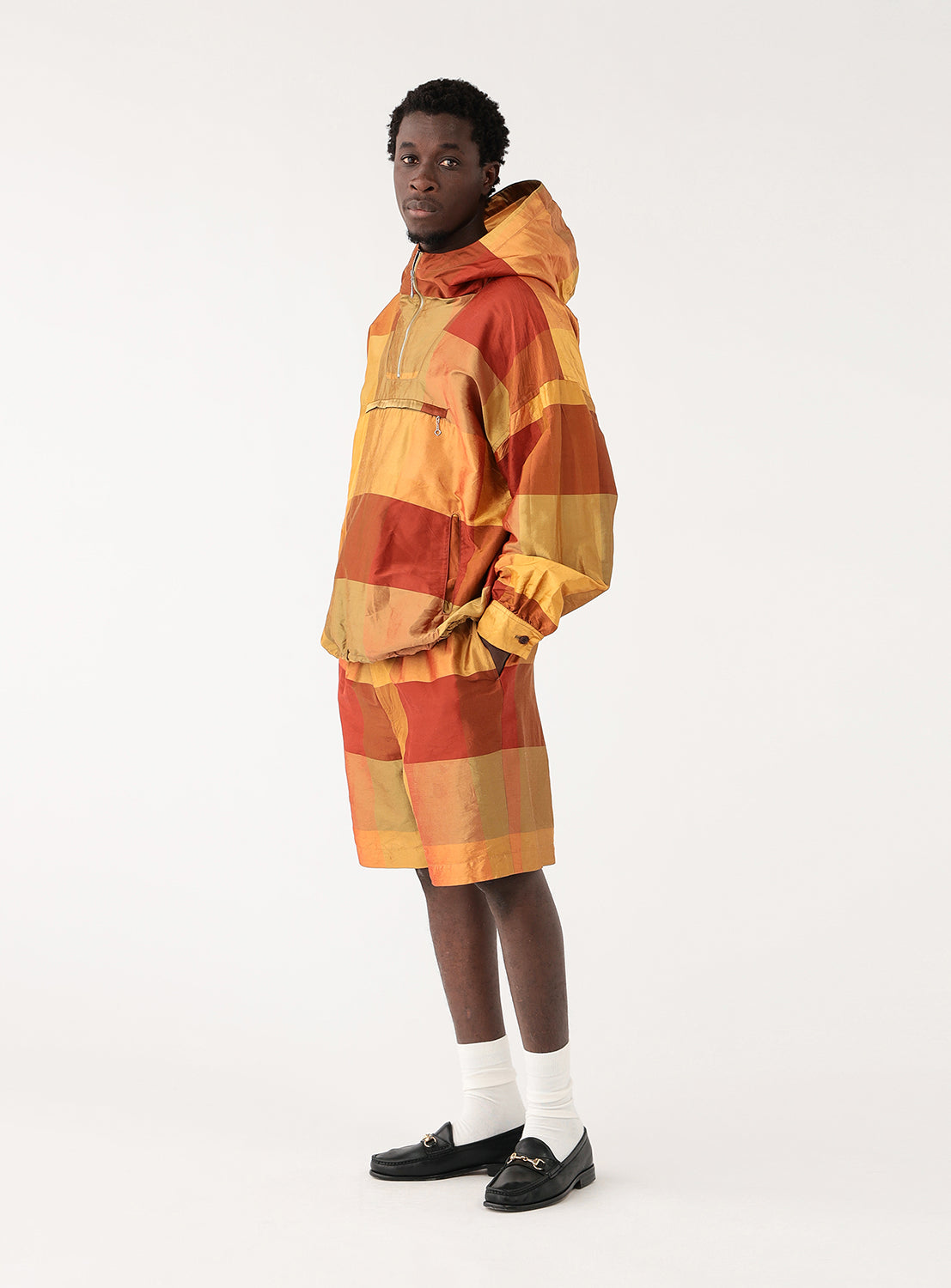 Model in orange and yellow block-patterned hoodie and matching shorts, side view, showcasing relaxed fit.