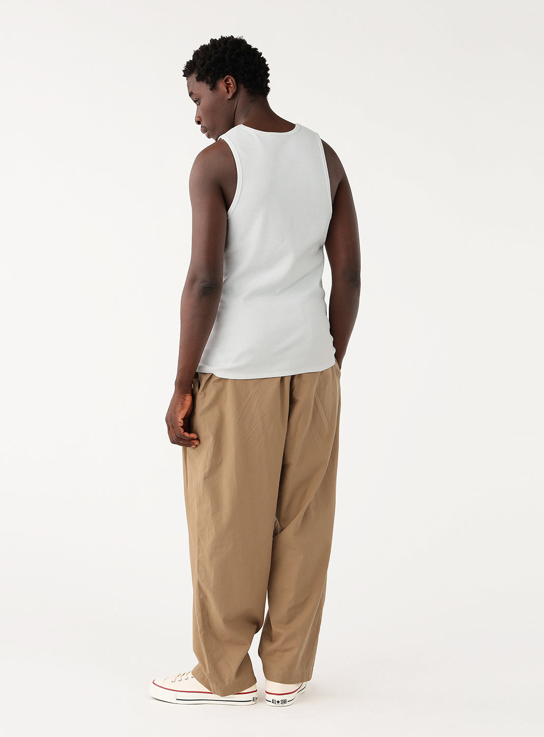 Front shot of a model in a white ribbed tank, paired with wide-leg beige pants and light sneakers.