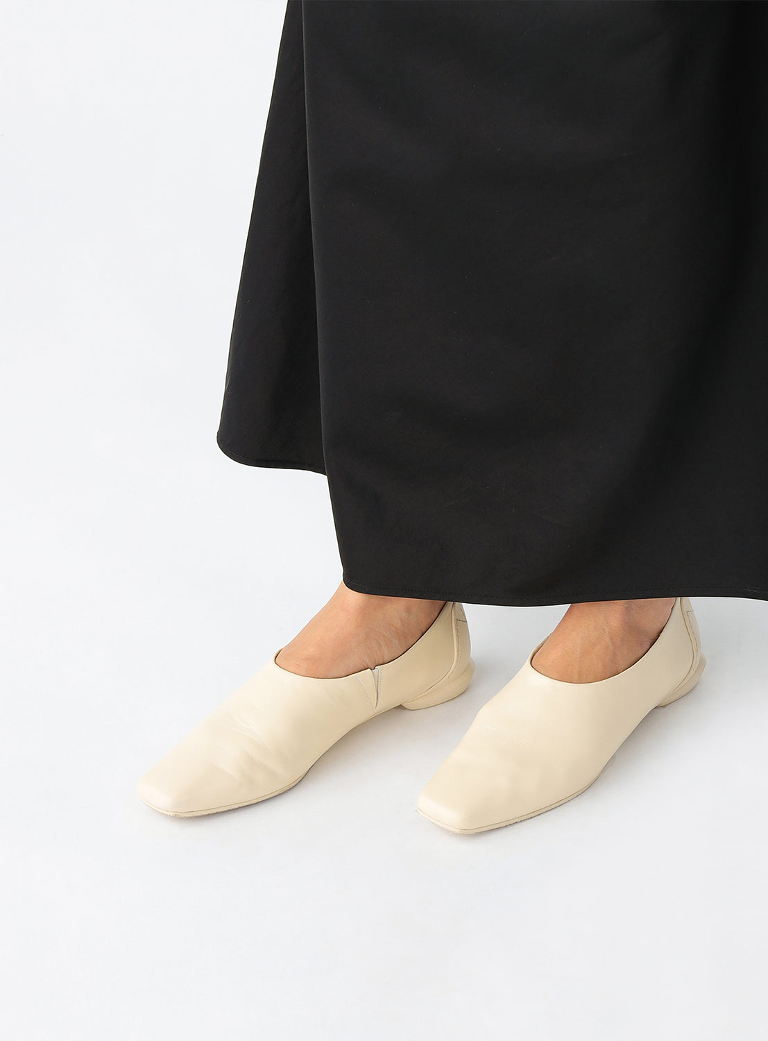 Model wearing ivory slip on square toe shoes.