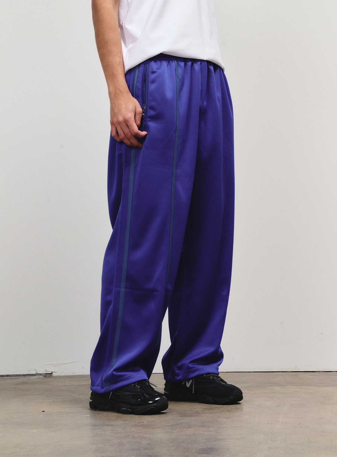 Close-up of blue track pants, showcasing distinctive side lines and a relaxed fit.