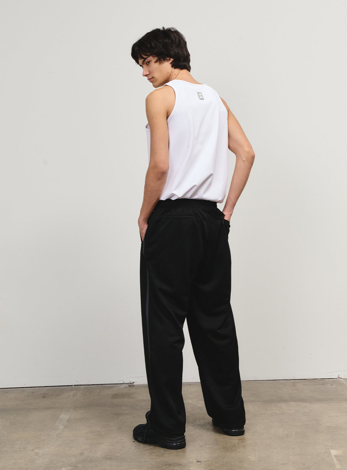 Back view of a model in black track pants, highlighting the full silhouette and understated design.