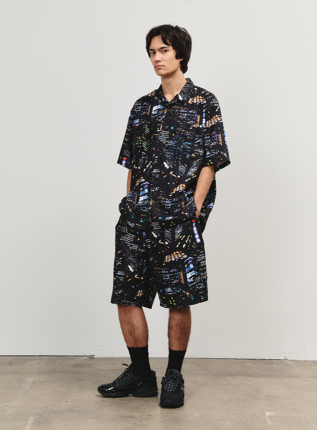 Model wearing shorts and a matching shirt with an all-over city nightscape print for a coordinated look.