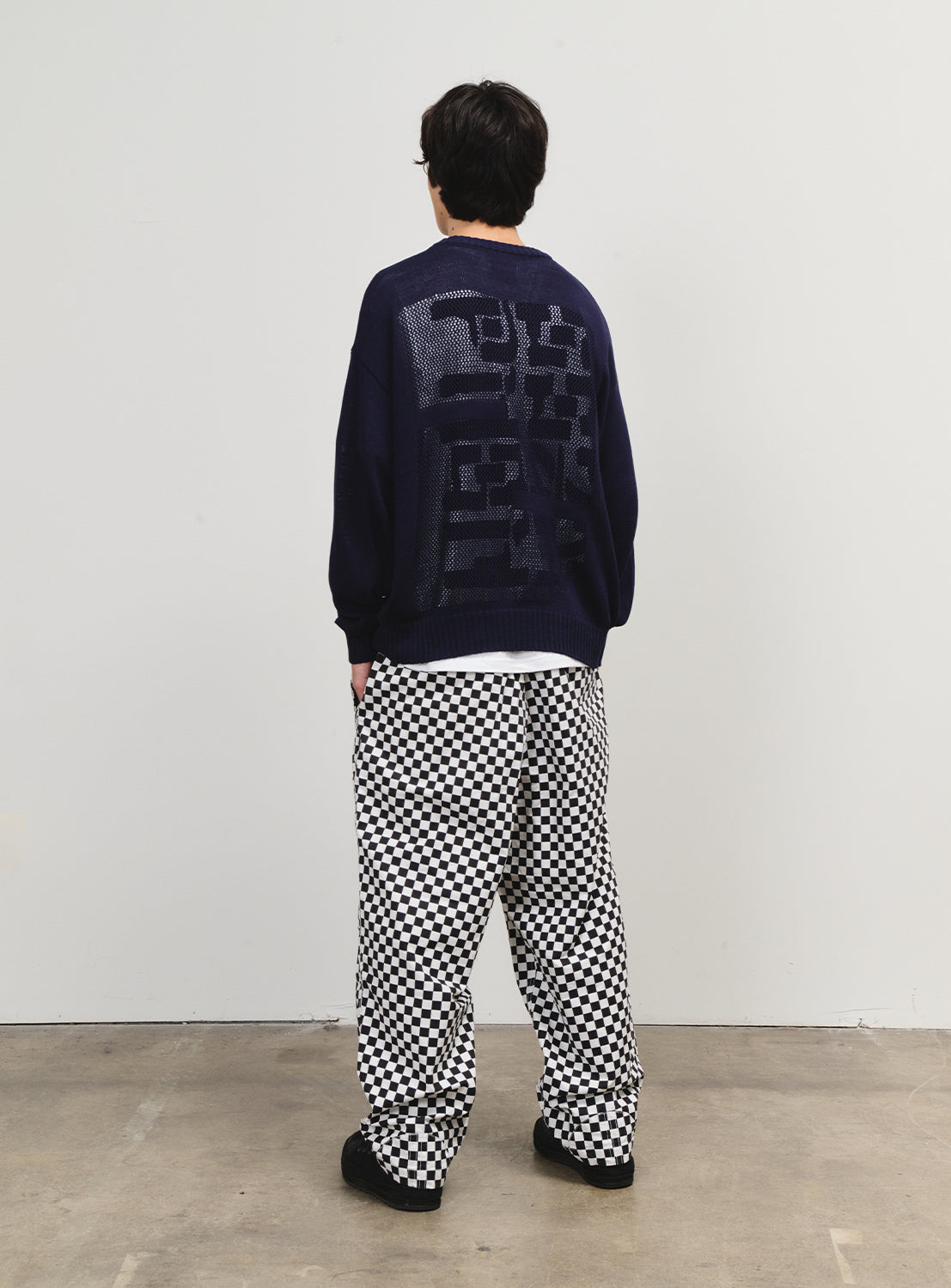Back of a model in black and white checkered pants, showcasing a loose fit and bold pattern.