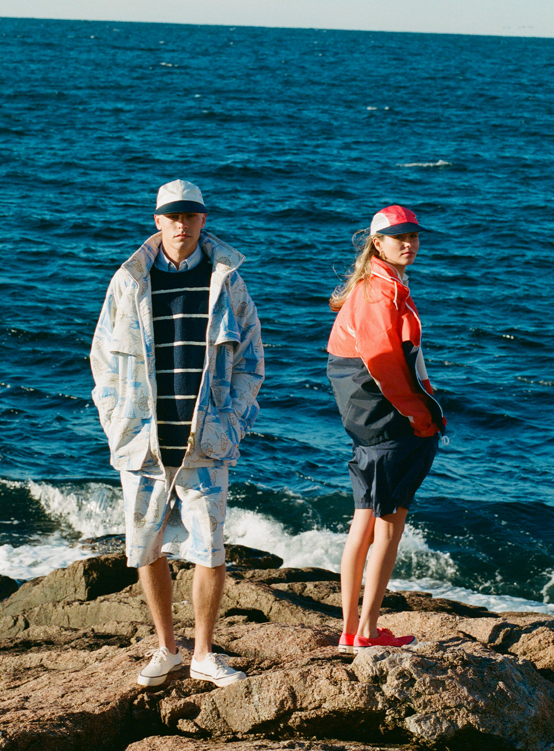 Two people standing on rocks by the ocean, one wearing the jacket and matching shorts.