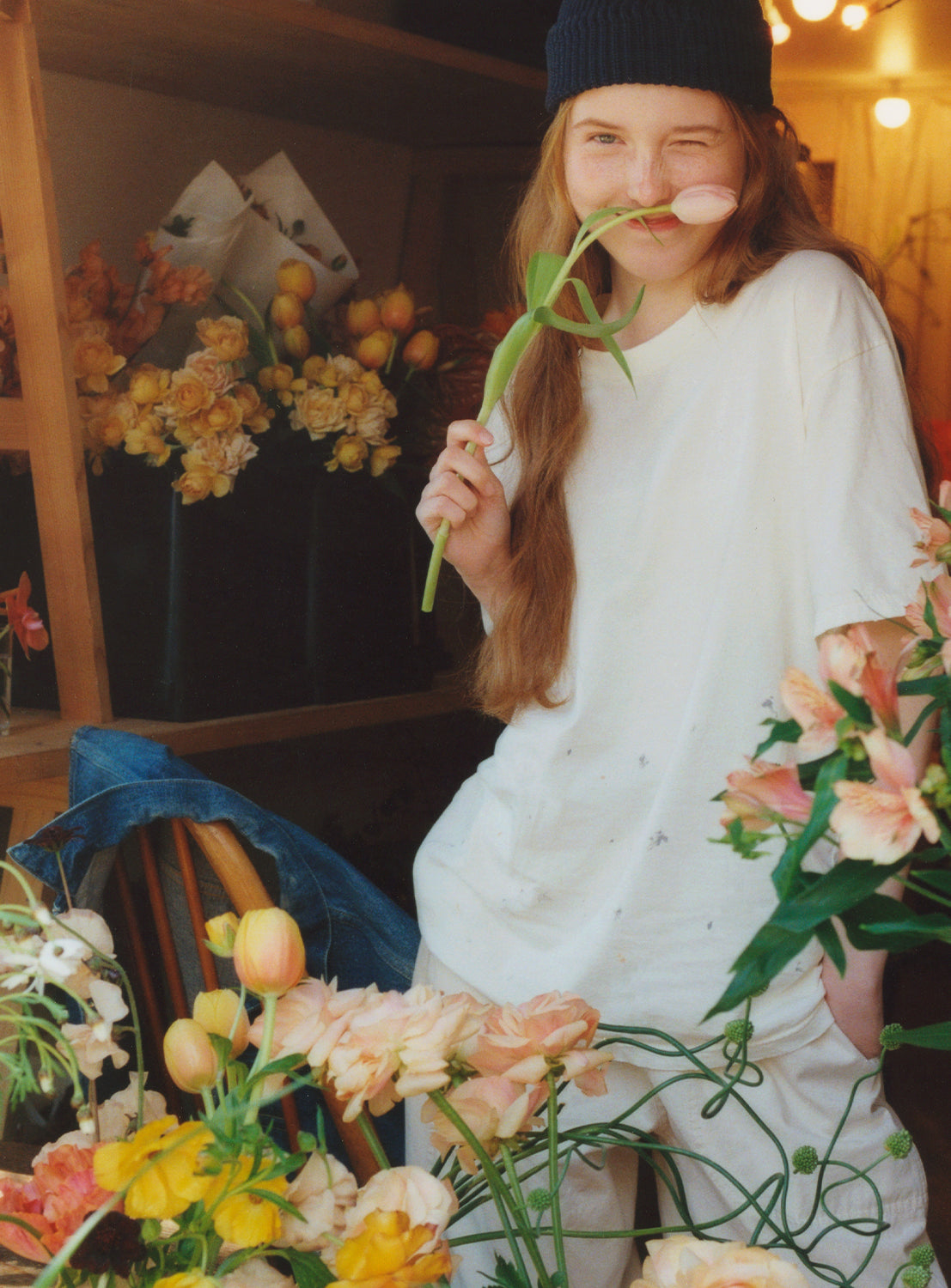 Model wearing a white crew neck t-shirt with a paint stain design hold a flower in a flower shop.