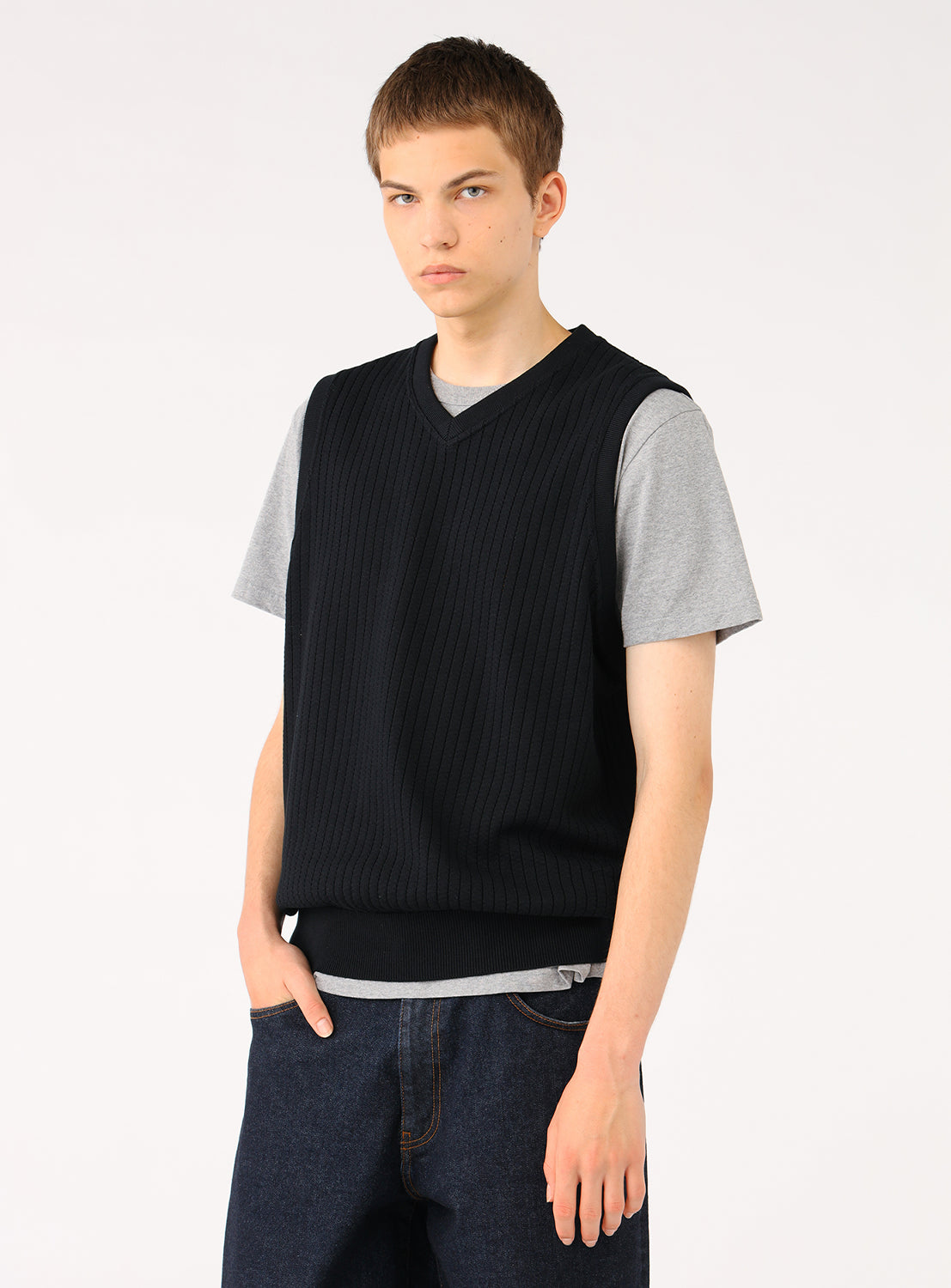 Model wearing a black ribbed knit vest over a grey t-shirt and blue jeans, front view.