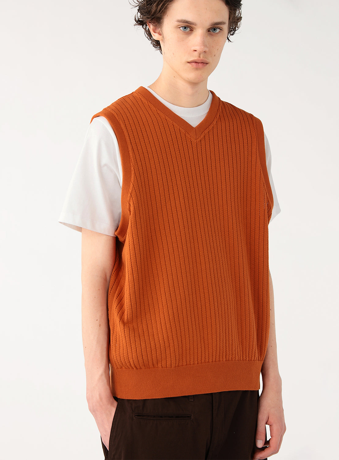 Model wearing a rust-colored ribbed knit vest over a white t-shirt and black pants, front view.
