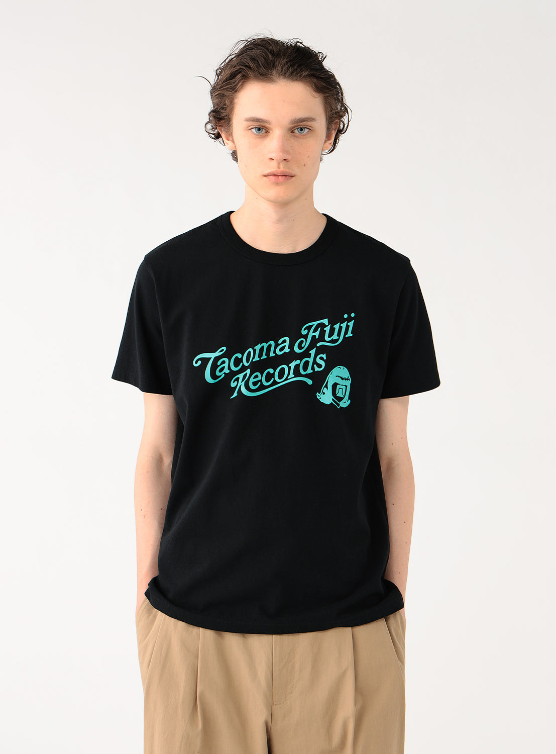 Model wearing a black t-shirt with mint green "Tacoma Fuji Records" graphic and khaki pants, front view.