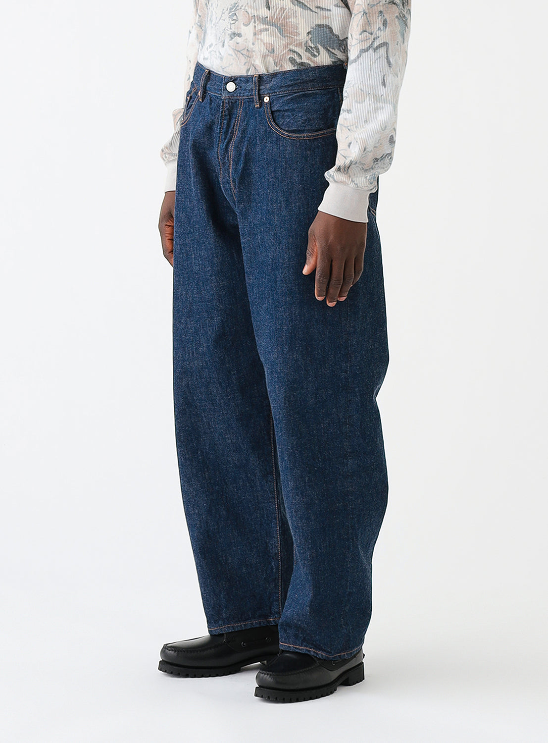 Side view of a model wearing a pair of dark blue denim wide fit pants.